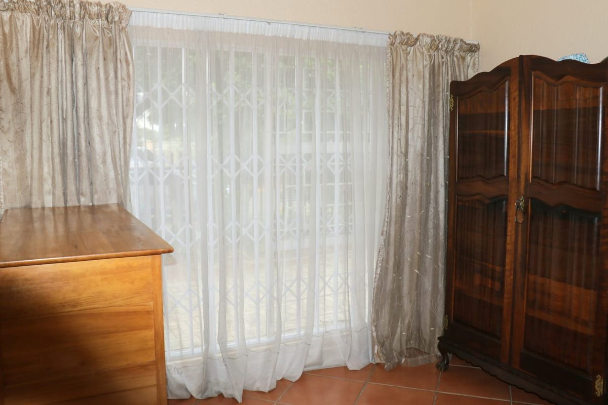 A bedroom featuring terracotta floor tiles and a large window fitted with a white security gate.