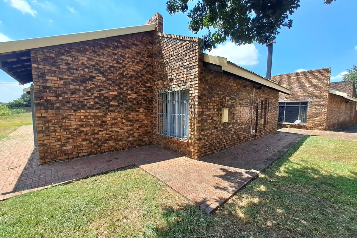 Rear view of the house featuring exposed face-brick exterior, paved walkway, and security bars on windows.