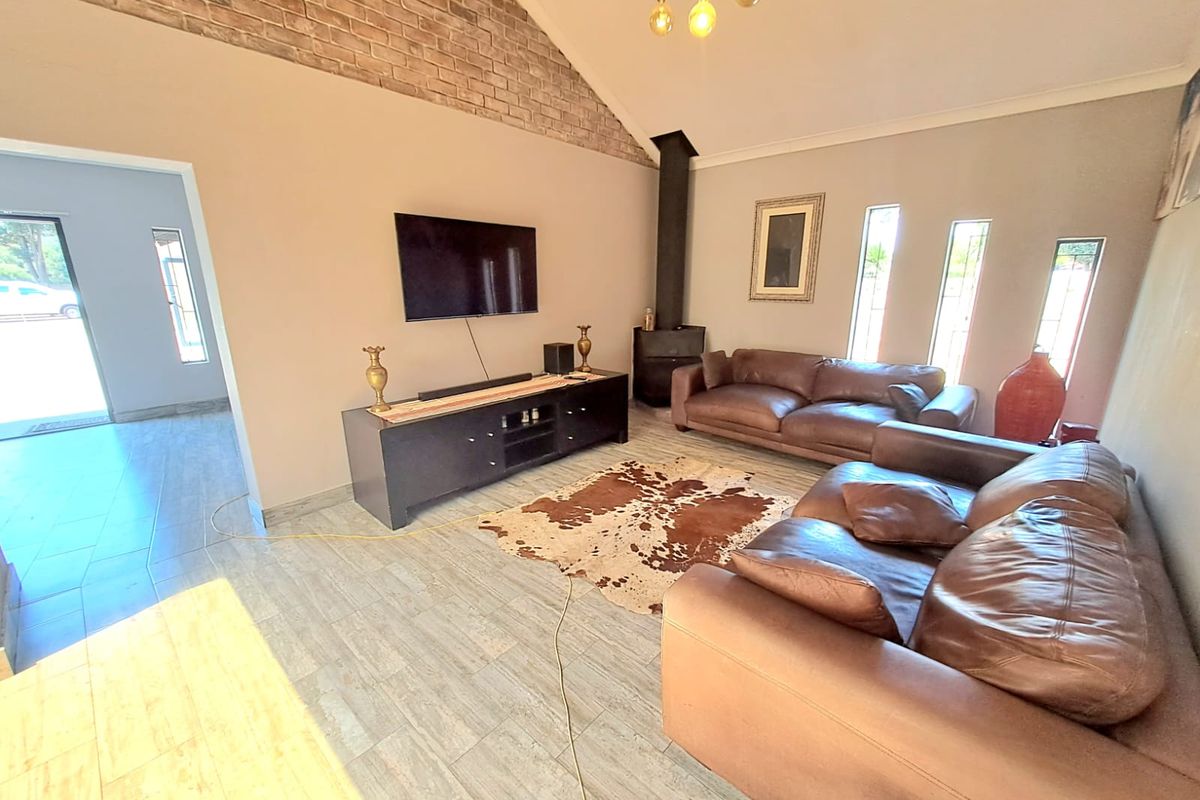 Spacious living room featuring a vaulted ceiling with exposed brick detail, tiled flooring, and a built-in fireplace.