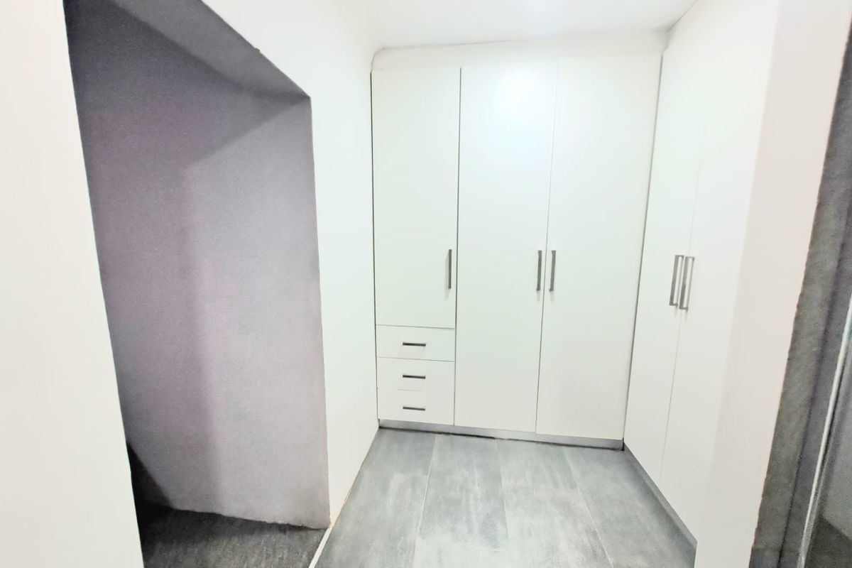 A clean and modern walk-in closet or dressing area featuring built-in white cabinetry with ample storage and sleek grey tiled flooring.