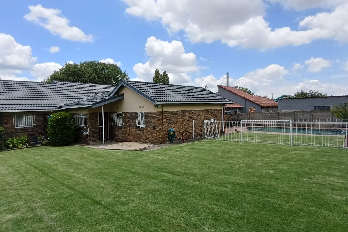 Rear view of the house featuring a well-maintained lawn, a fenced swimming pool area, and brick exterior walls with tiled roofing.