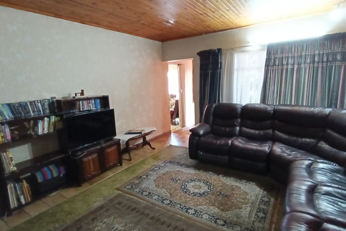 A living room featuring a timber-clad ceiling, tiled flooring, and a doorway leading to an adjacent room.