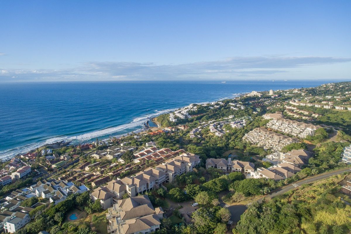 Aerial view of a coastal residential estate featuring lush greenery, multi-story housing complexes, and direct proximity to the ocean coastline.