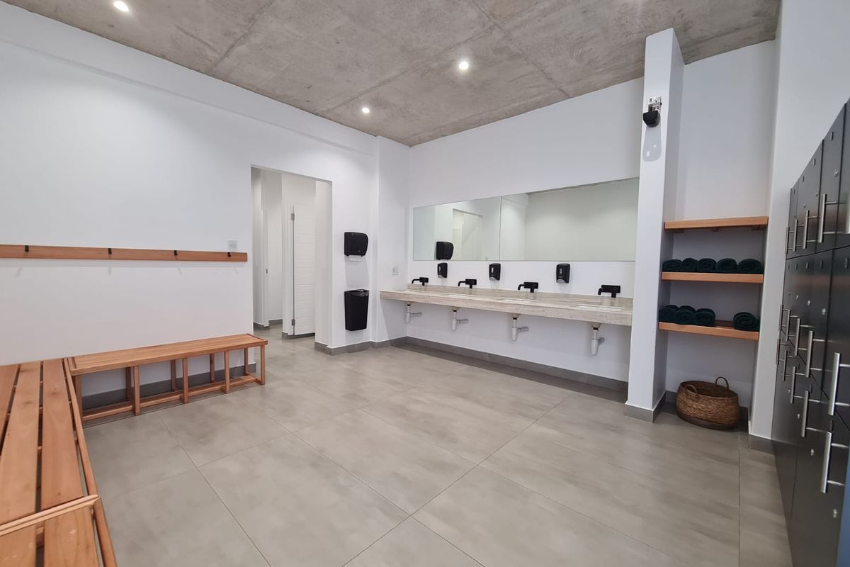 Modern communal bathroom or changing area featuring a concrete ceiling, tiled flooring, multiple vanity basins, and built-in storage lockers.