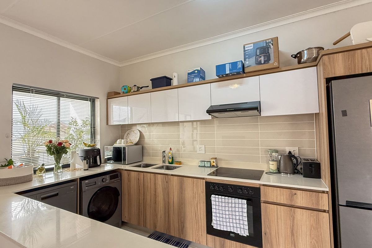 Modern kitchen featuring wood-grain cabinetry, white upper cabinets, stone countertops, integrated oven, hob, extractor fan, and a dedicated space for laundry appliances.