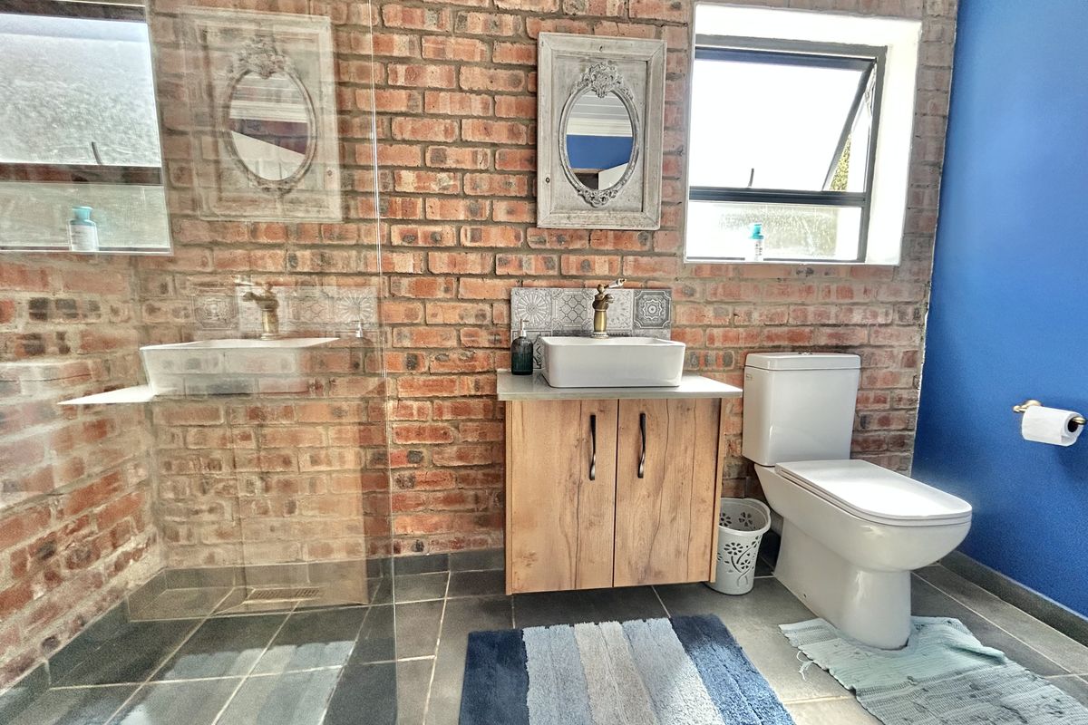 A modern bathroom featuring an exposed brick feature wall, a floating vanity with a vessel sink, a glass-enclosed shower, and a contemporary toilet.