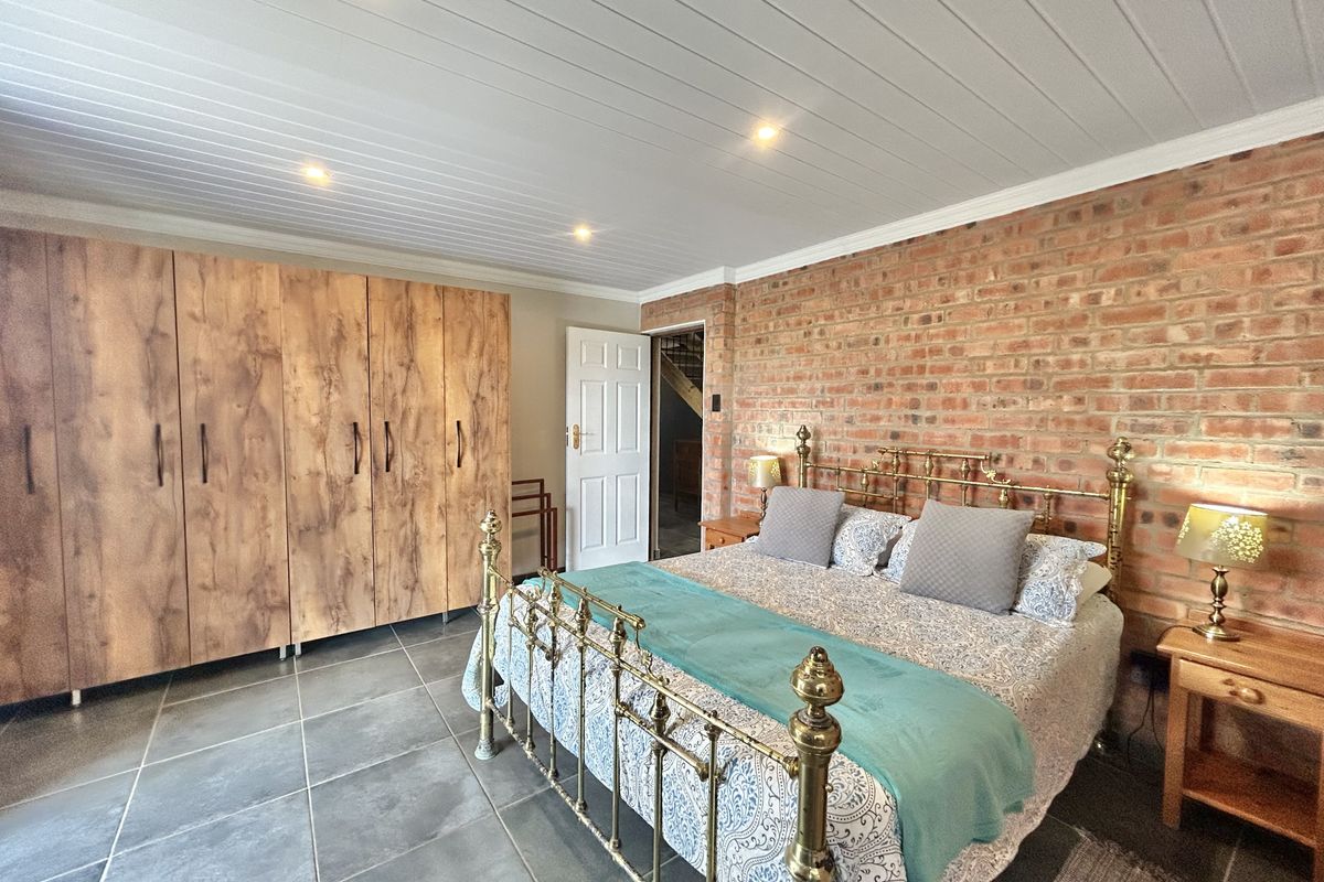 Spacious bedroom featuring a rustic exposed brick feature wall, built-in wooden cabinetry, tiled flooring, and a white tongue-and-groove ceiling with recessed lighting.