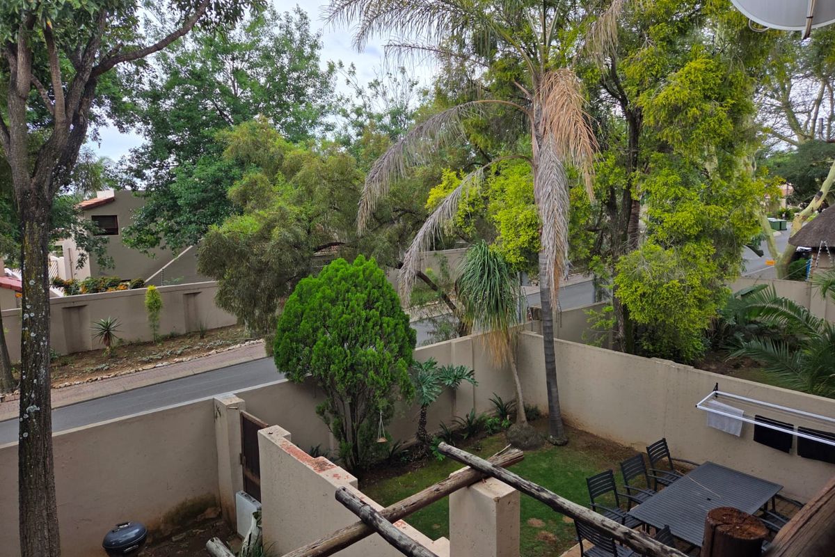 Elevated view of a private garden area featuring a paved patio, timber pergola structure, and established trees within a walled perimeter.