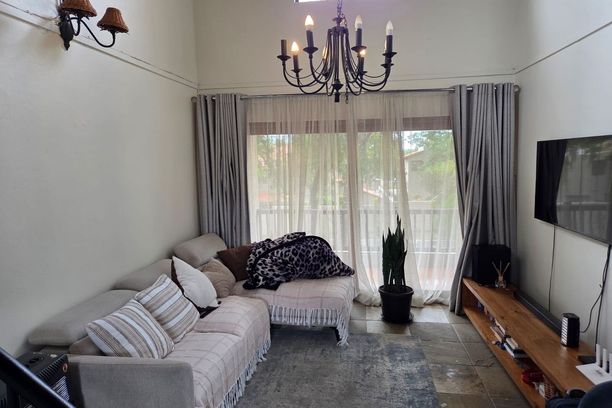 A cozy living room featuring high ceilings, a decorative chandelier, stone flooring, and large sliding glass doors leading to a balcony.