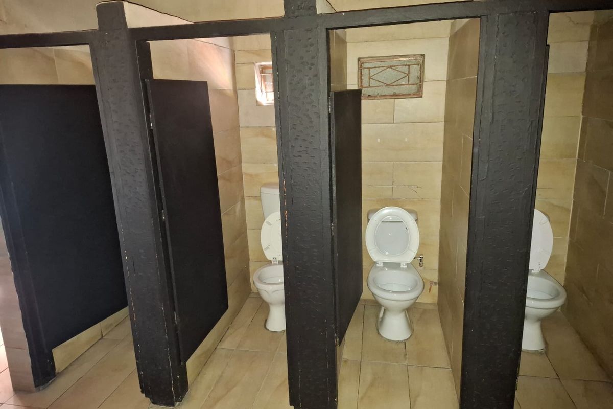 Communal bathroom facility featuring multiple toilet stalls with dark timber partitions and tiled flooring.