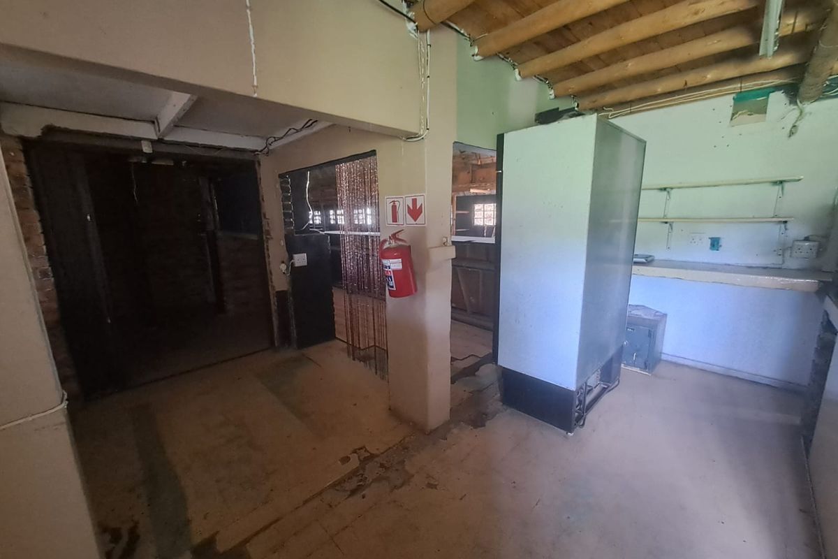 A rustic, unfinished utility or kitchen area featuring exposed timber ceiling beams, concrete flooring, and basic wall-mounted shelving in a farm-style property.