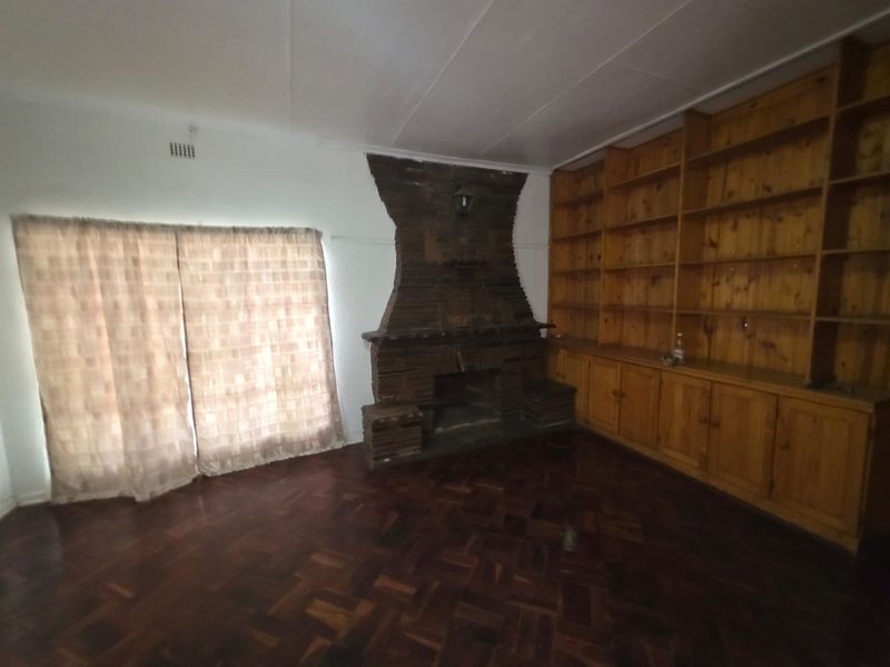 Spacious living room featuring a prominent brick fireplace, extensive built-in wooden shelving, and traditional parquet flooring.