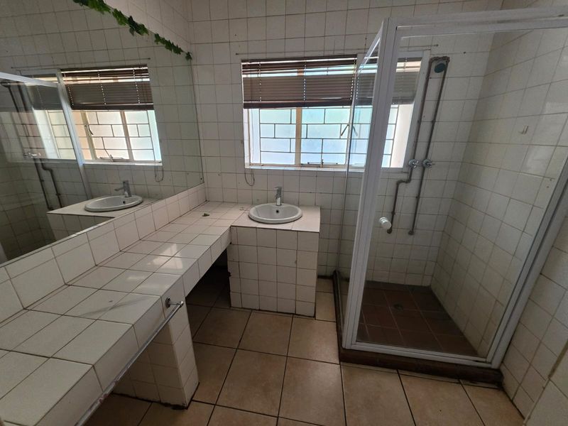 A dated bathroom featuring a tiled vanity with a drop-in basin, a separate shower enclosure, and full-height wall tiling.