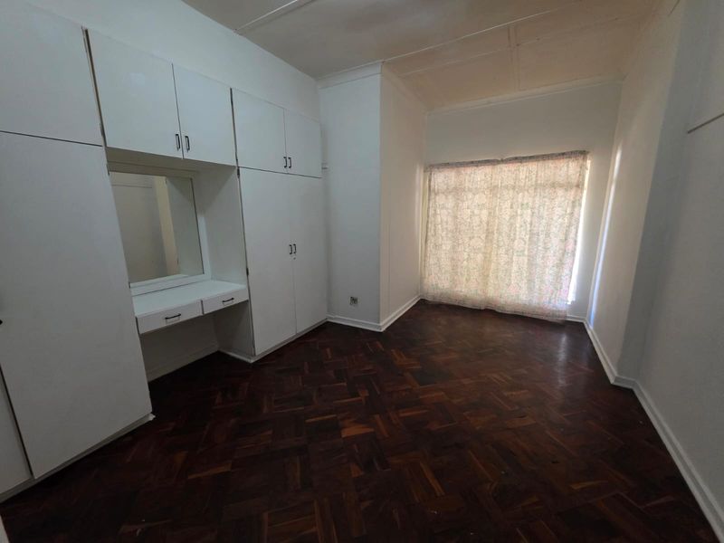 A vacant bedroom featuring classic parquet flooring, extensive built-in cupboard storage, and a integrated vanity unit.
