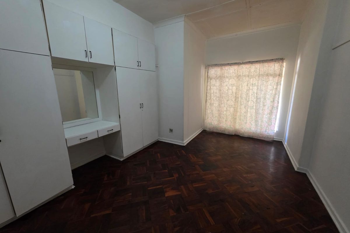 A vacant bedroom featuring classic parquet flooring, extensive built-in cupboard storage, and a integrated vanity unit.