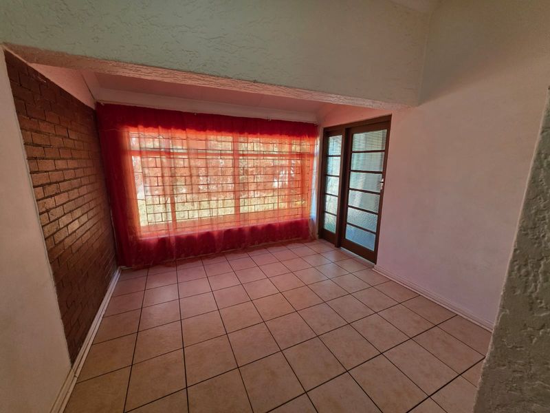An empty living area featuring tiled flooring, an exposed brick feature wall, and a glass door providing access to the exterior.
