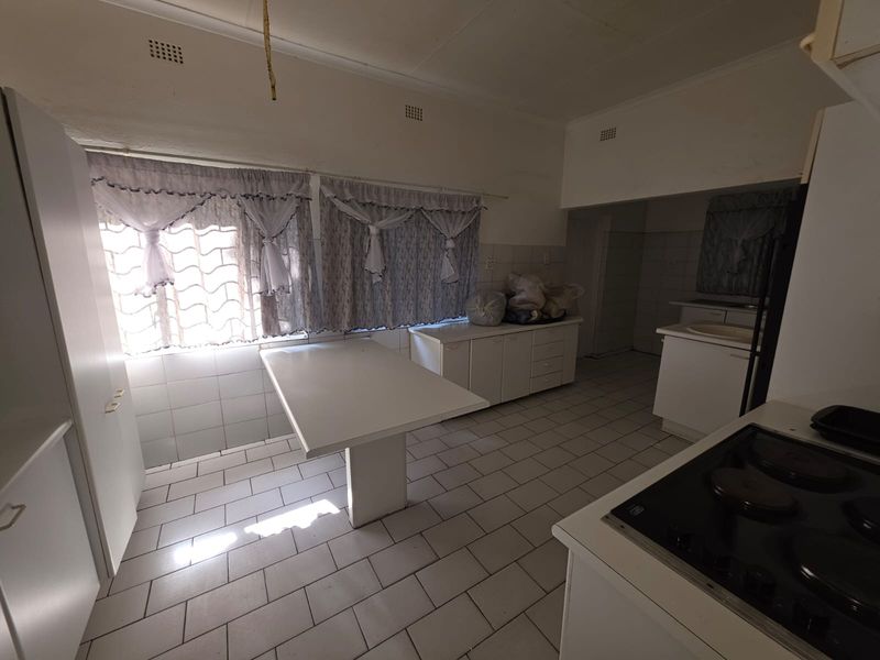 A dated kitchen featuring tiled flooring, built-in cabinetry, a fixed breakfast counter, and a built-in hob, offering significant potential for modernization.