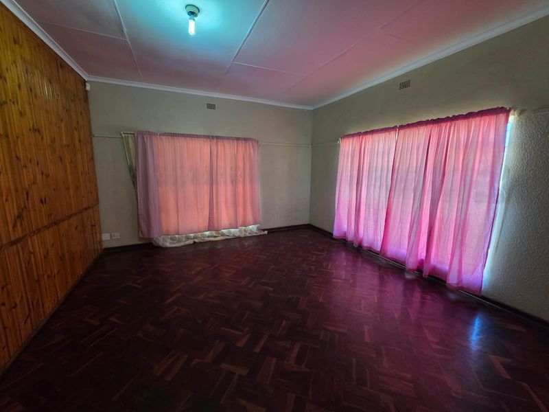Spacious living area featuring traditional parquet flooring and timber wall paneling, offering a blank canvas for renovation and modern interior design updates.