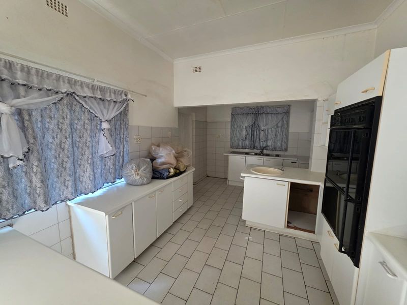 A dated kitchen featuring white cabinetry, tiled flooring, a double wall oven, and dual sink areas, offering significant potential for modernization and renovation.