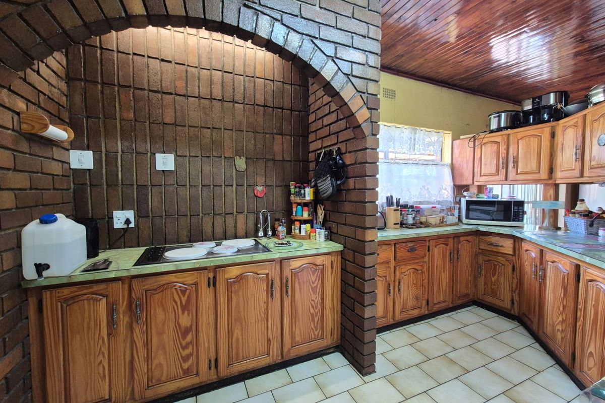 A traditional kitchen featuring solid wood cabinetry, a distinctive brick archway over the cooktop, tiled countertops, and a timber-paneled ceiling.