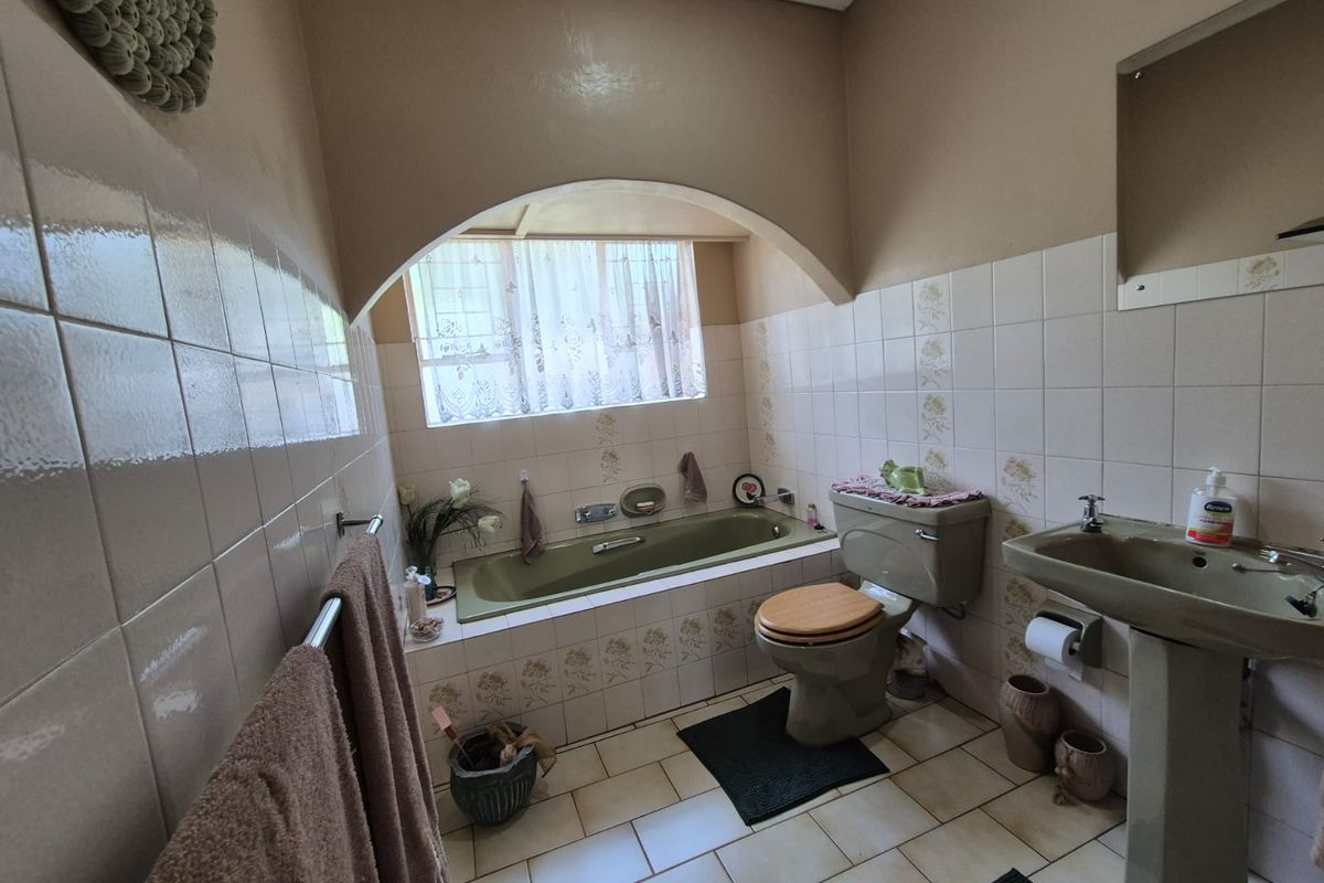 A dated bathroom featuring a built-in bathtub, pedestal sink, and toilet, finished with neutral wall tiles and ceramic floor tiles.