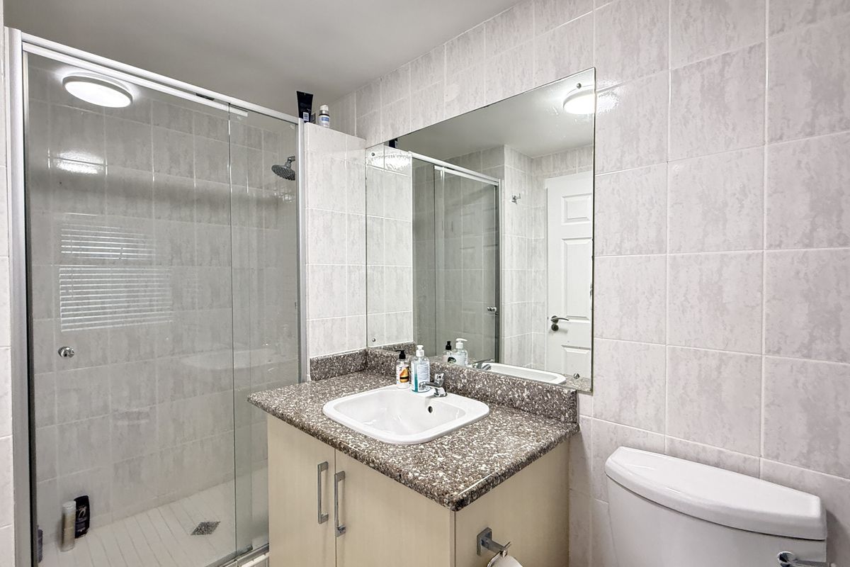 A functional bathroom featuring a glass-enclosed shower, a vanity with a stone-look countertop, a wall-mounted mirror, and a standard toilet.