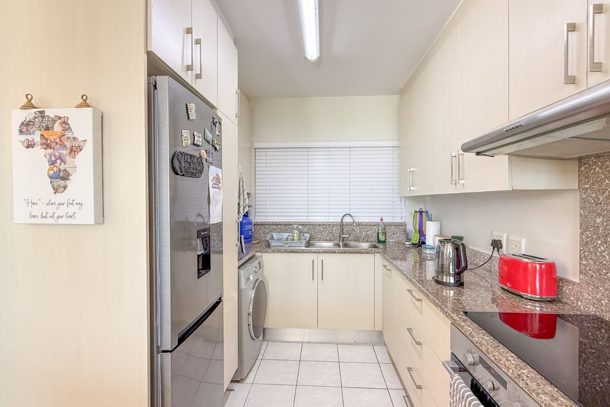 A functional galley-style kitchen featuring granite countertops, built-in cabinetry, a stainless steel extractor fan, and a dedicated space for a washing machine.
