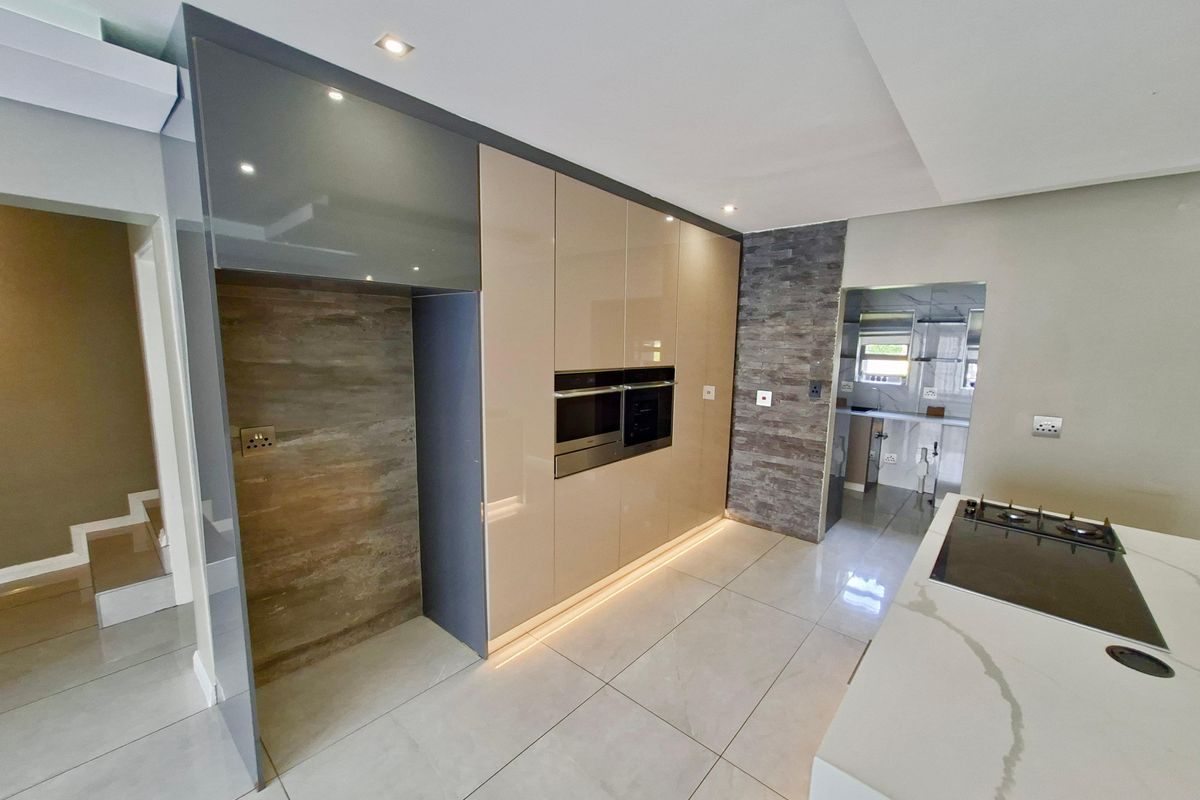 Modern kitchen featuring high-gloss cabinetry, built-in appliances, stone feature wall, and a central island with a gas hob and stone countertop.