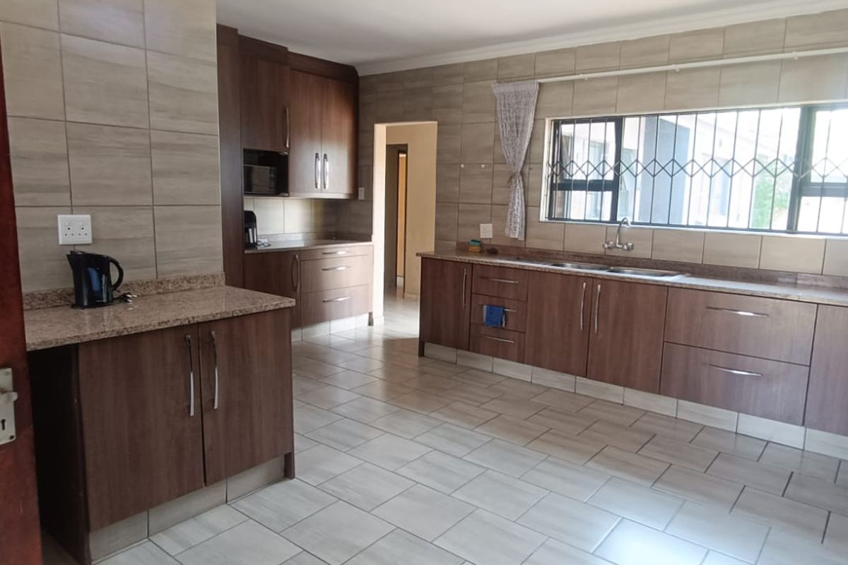 A spacious kitchen featuring wood-finish cabinetry, granite countertops, tiled flooring, and a large window with security bars.