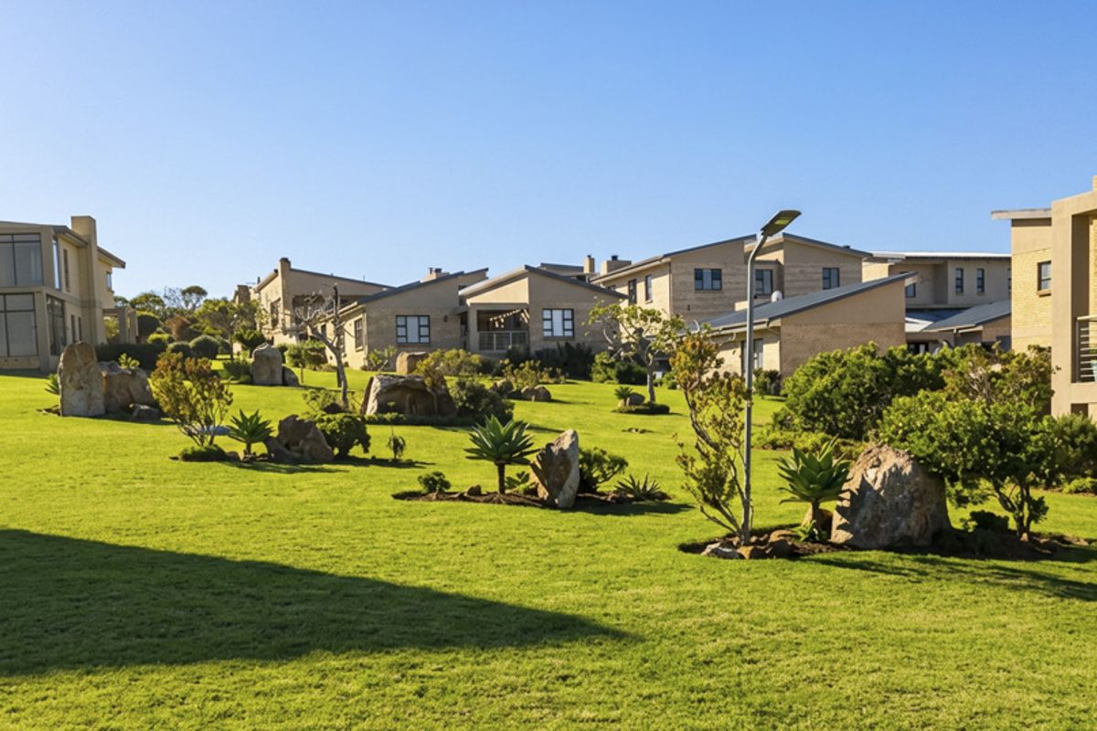 A well-maintained communal garden area featuring manicured lawns, decorative boulder rock formations, and established landscaping within a residential estate setting.