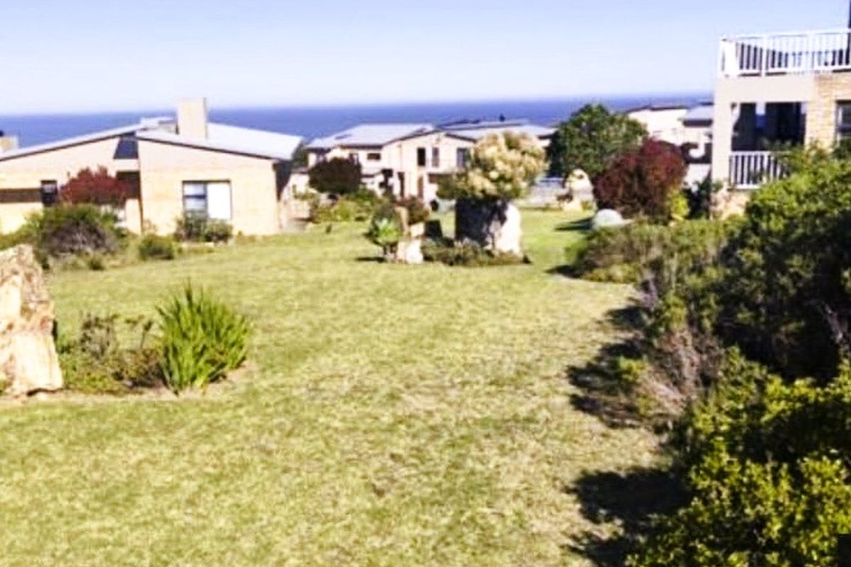 A well-maintained residential garden area featuring established lawn and shrubbery with surrounding neighborhood homes and distant ocean views.