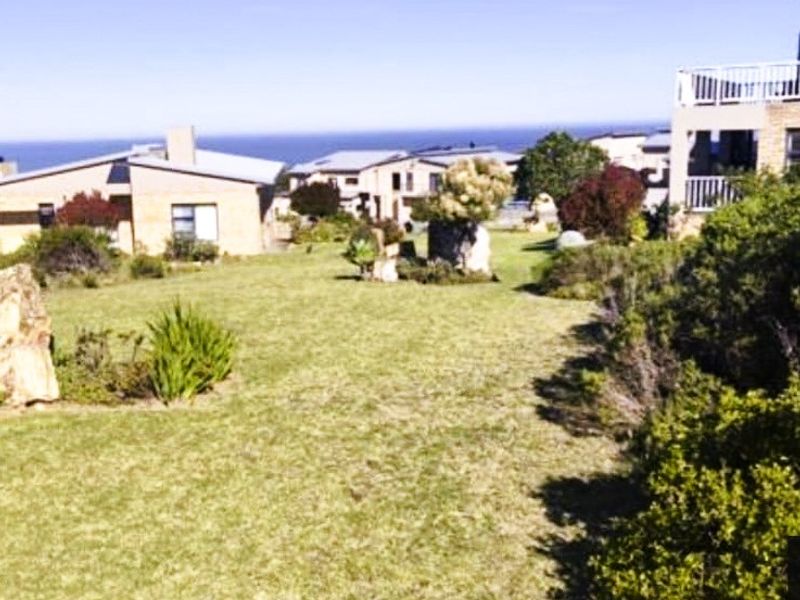 A well-maintained residential garden area featuring established lawn and shrubbery with surrounding neighborhood homes and distant ocean views.