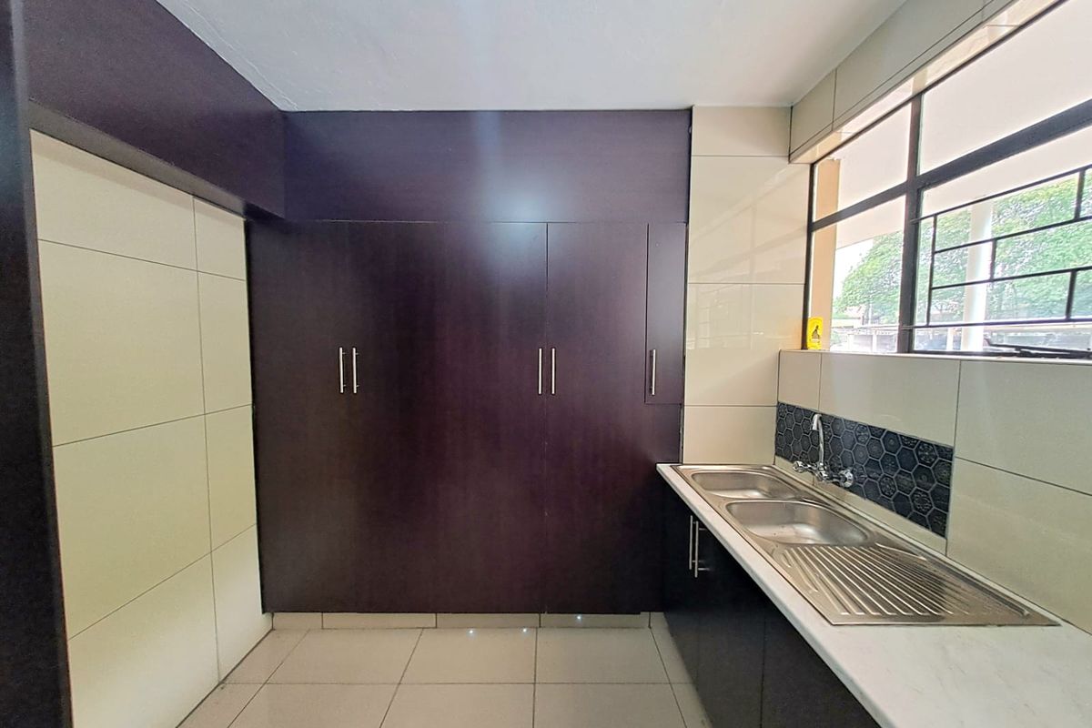 A functional kitchen featuring dark cabinetry, a double stainless steel sink, and tiled splashbacks with large format floor tiles.