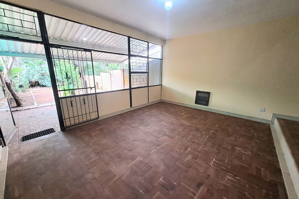 An empty living area featuring parquet flooring, large windows with security bars, and direct access to an outdoor patio space.