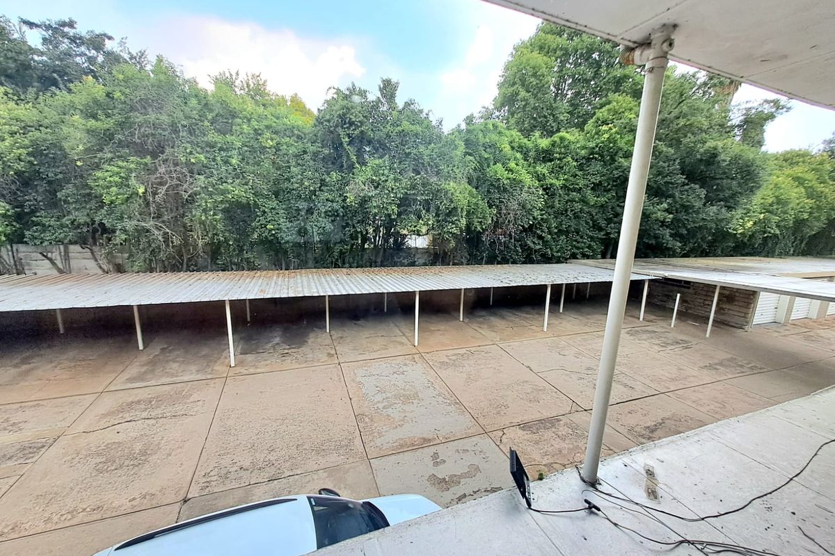 An elevated view of a communal parking area featuring a long metal carport structure and concrete paving, viewed from an adjacent balcony.