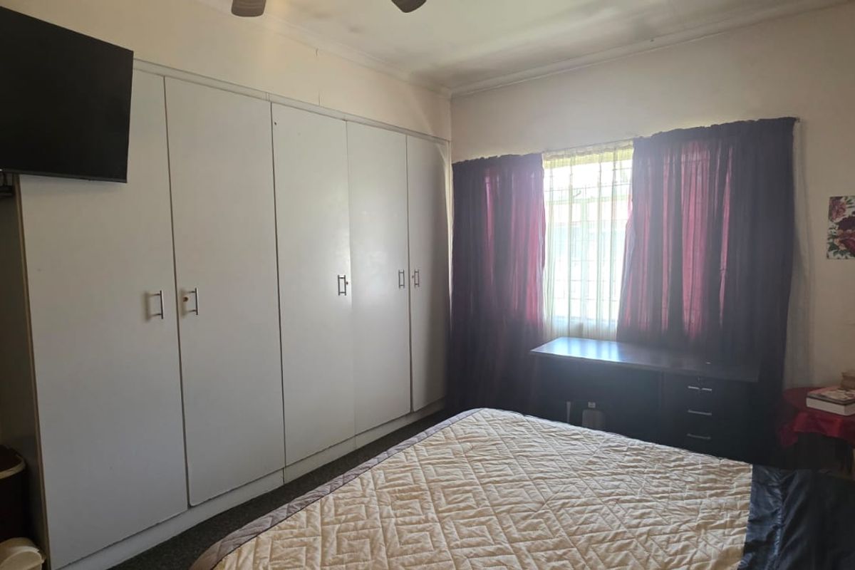A bedroom featuring built-in floor-to-ceiling wardrobes, a window with security bars, and a ceiling fan.