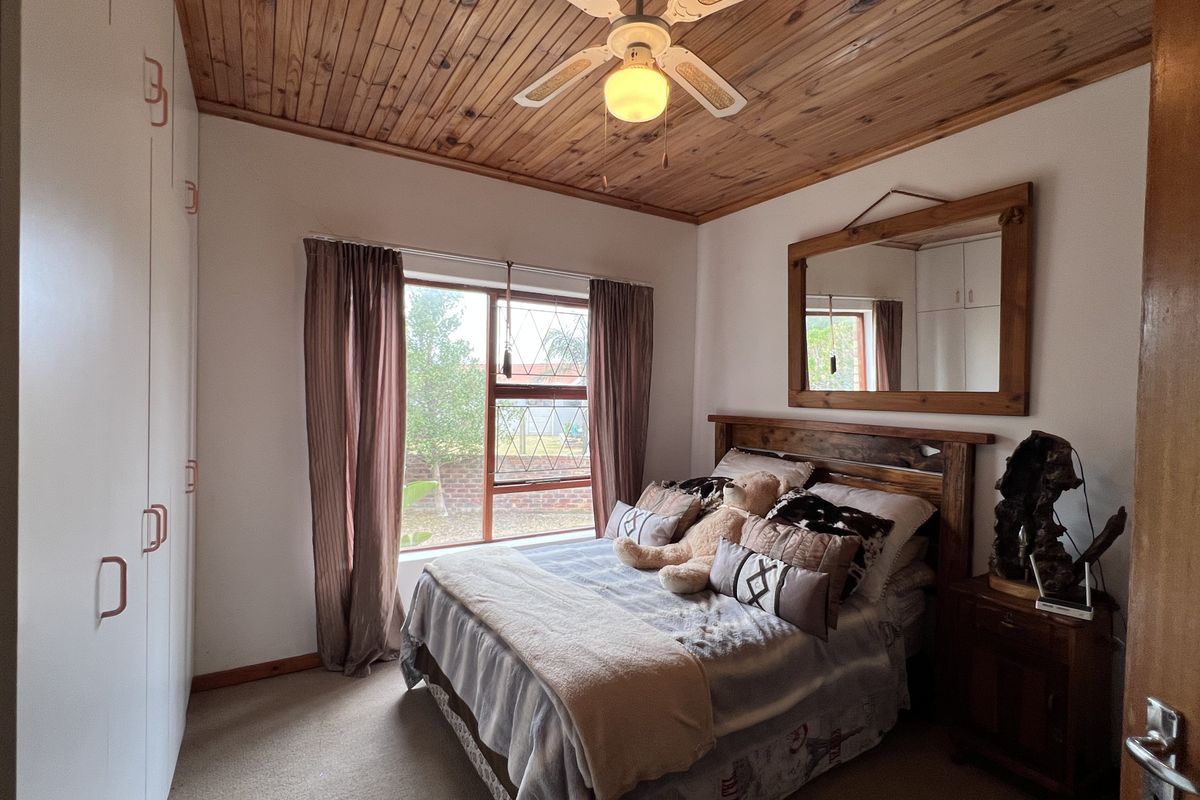 A cozy bedroom featuring a timber-clad ceiling, ceiling fan, built-in wardrobes, and a large window providing natural light.