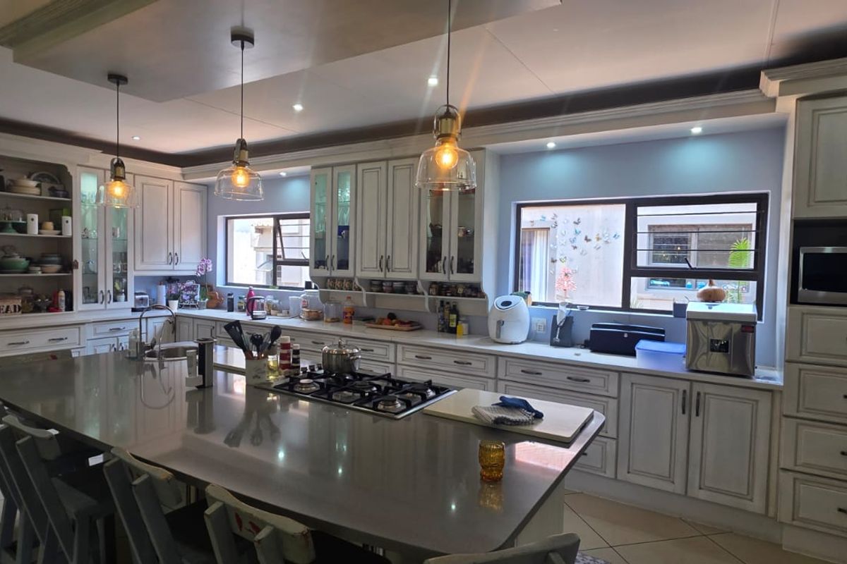 Spacious kitchen featuring custom cabinetry, a large central island with a built-in gas hob, stone countertops, and integrated lighting.