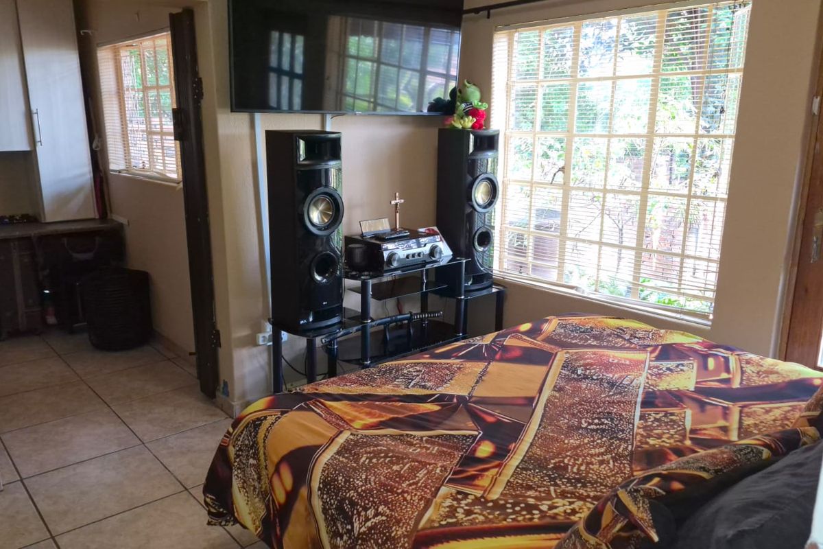 A bedroom featuring tiled flooring and large windows, with an adjacent kitchenette area visible in the background.