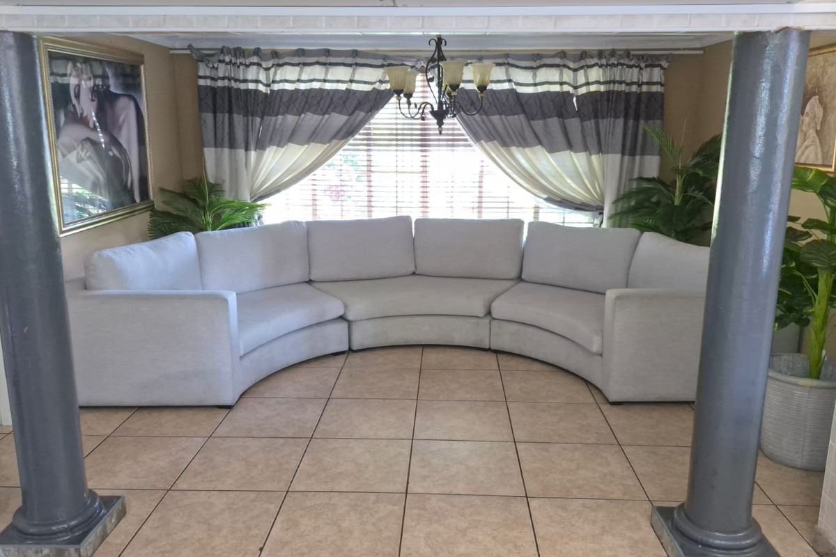 A living room area featuring tiled flooring, decorative columns, and a large window with integrated blinds.