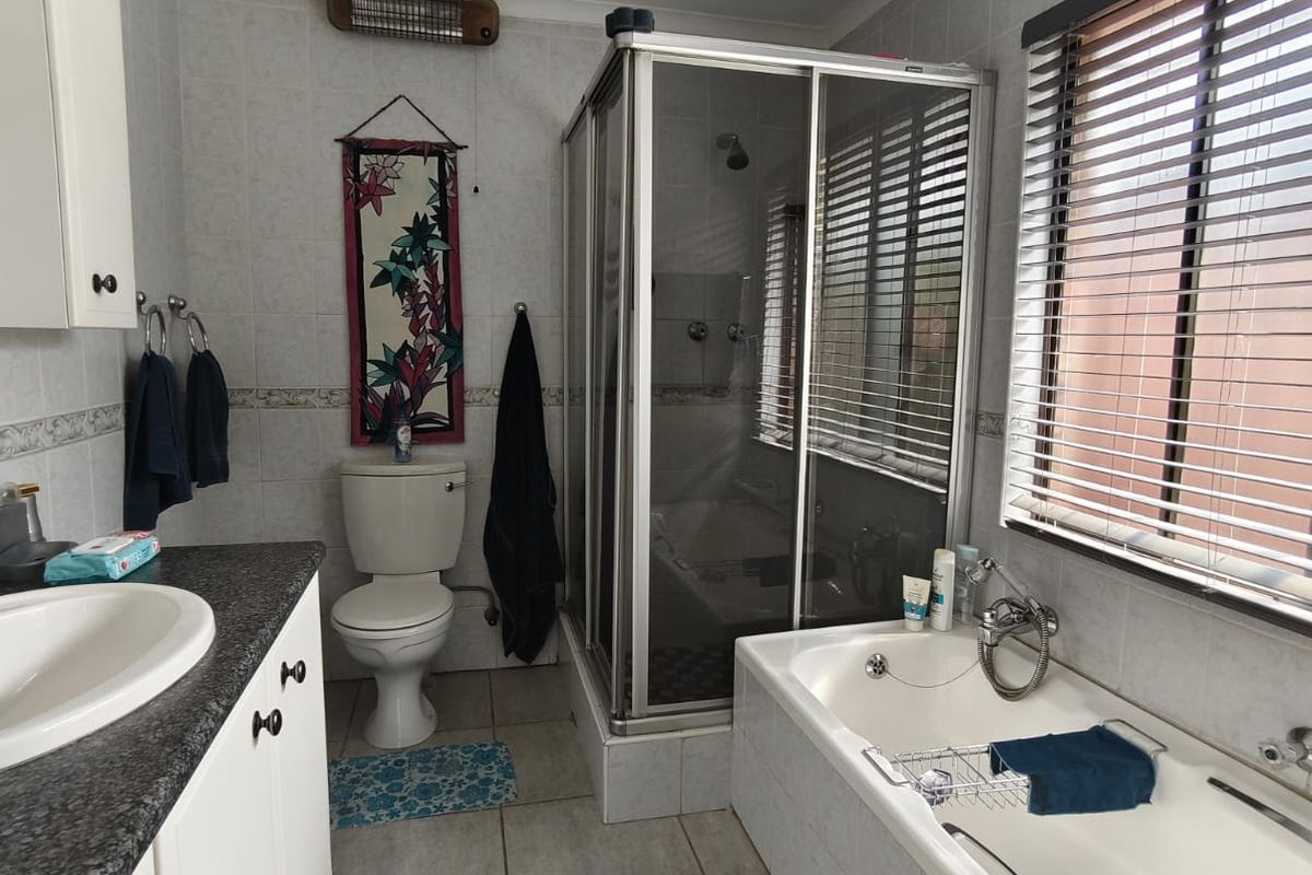 A functional bathroom featuring a built-in vanity, a separate shower enclosure, and a bathtub with tiled surrounds and window blinds.