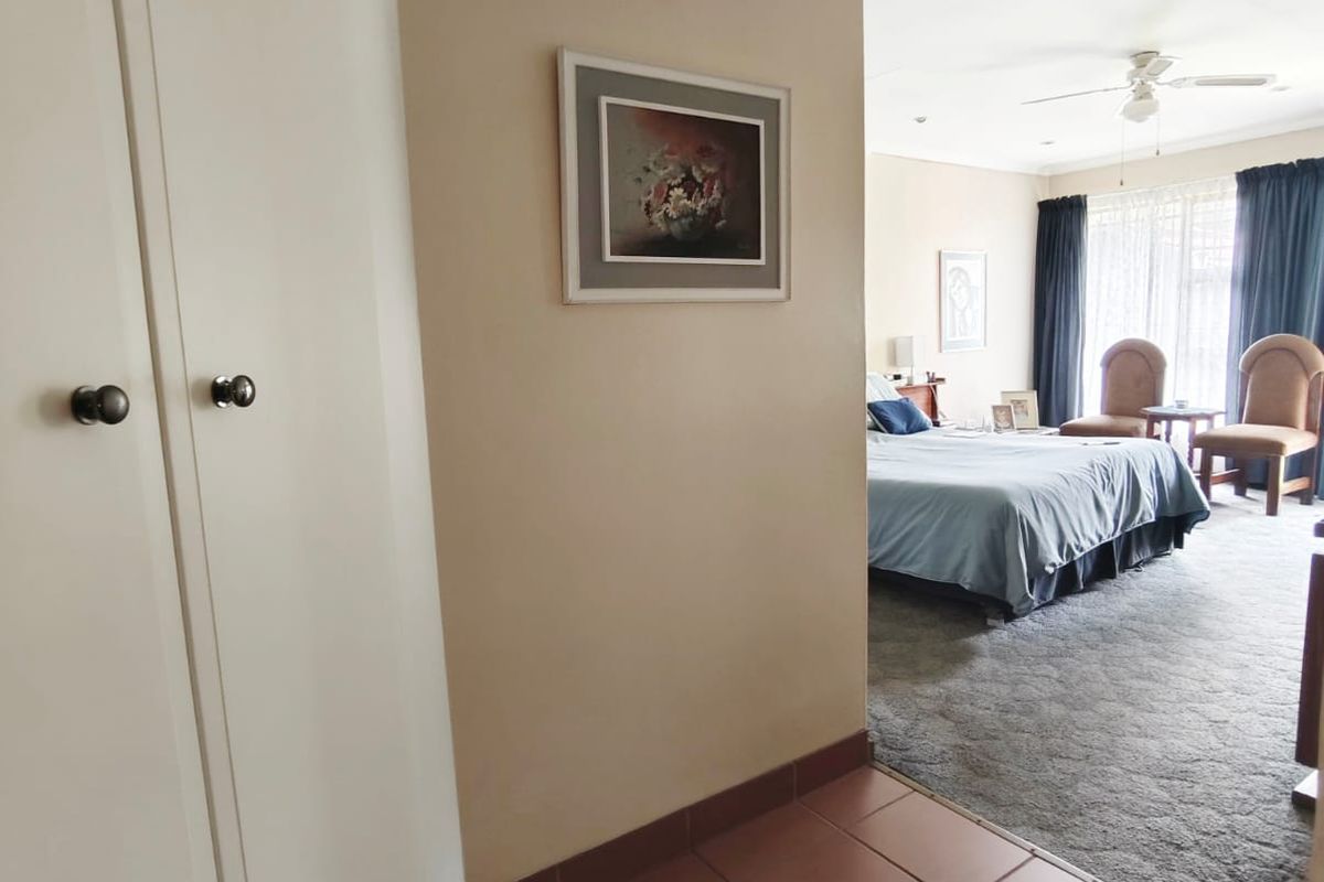 A view from a tiled hallway into a carpeted bedroom featuring built-in cupboards and a ceiling fan.