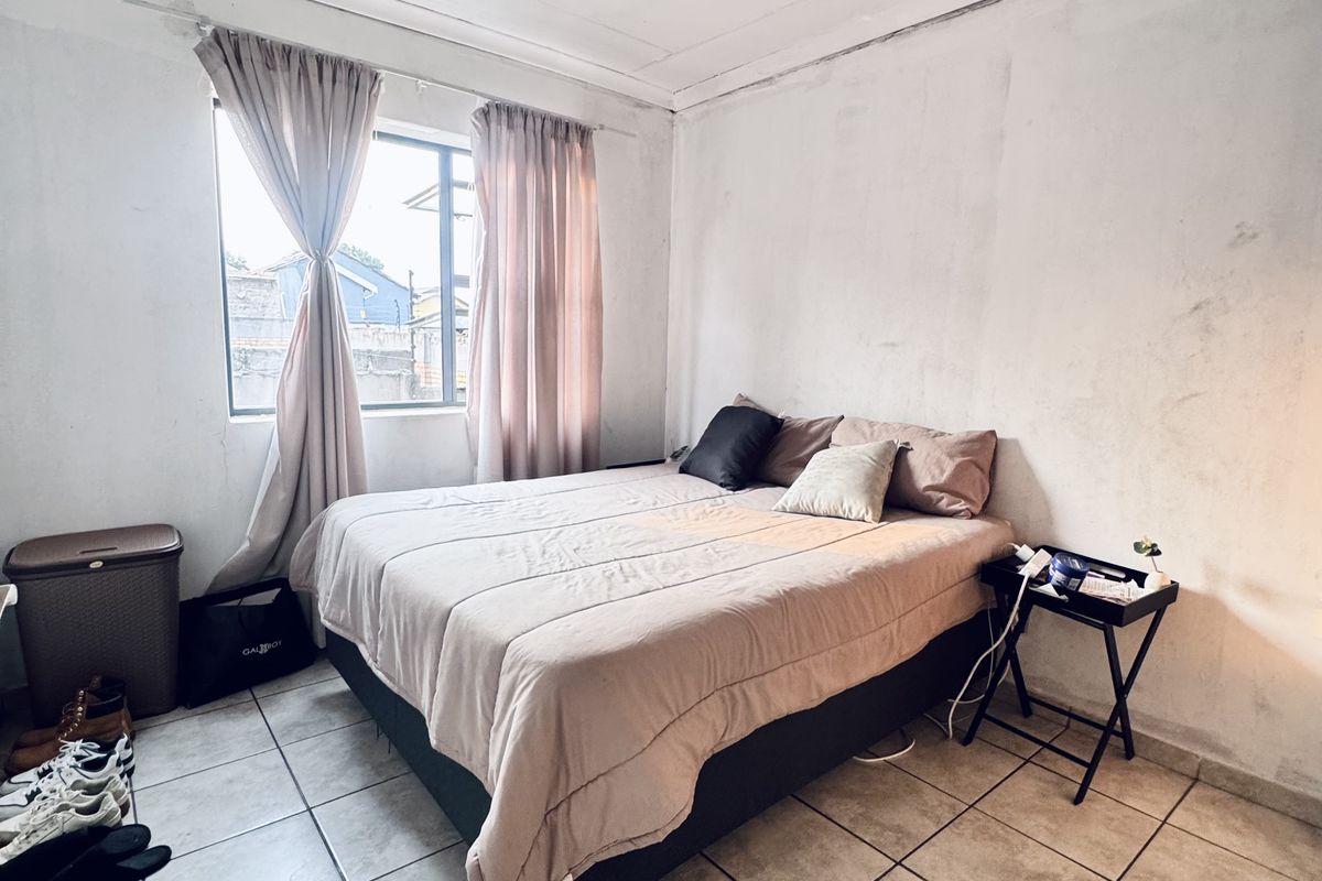 A bedroom featuring tiled flooring and a window with curtains. The walls show signs of wear and require cosmetic attention.