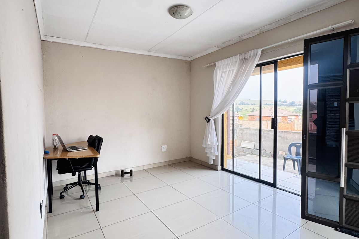 A bright living room featuring large sliding glass doors that open onto an outdoor patio area, finished with neutral floor tiles.
