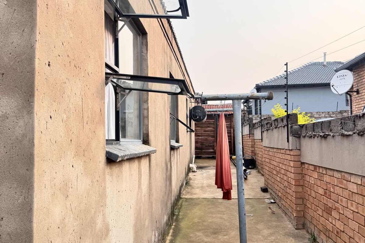 A narrow side exterior area featuring concrete paving, a brick boundary wall with electric fencing, and metal top-hung window frames.