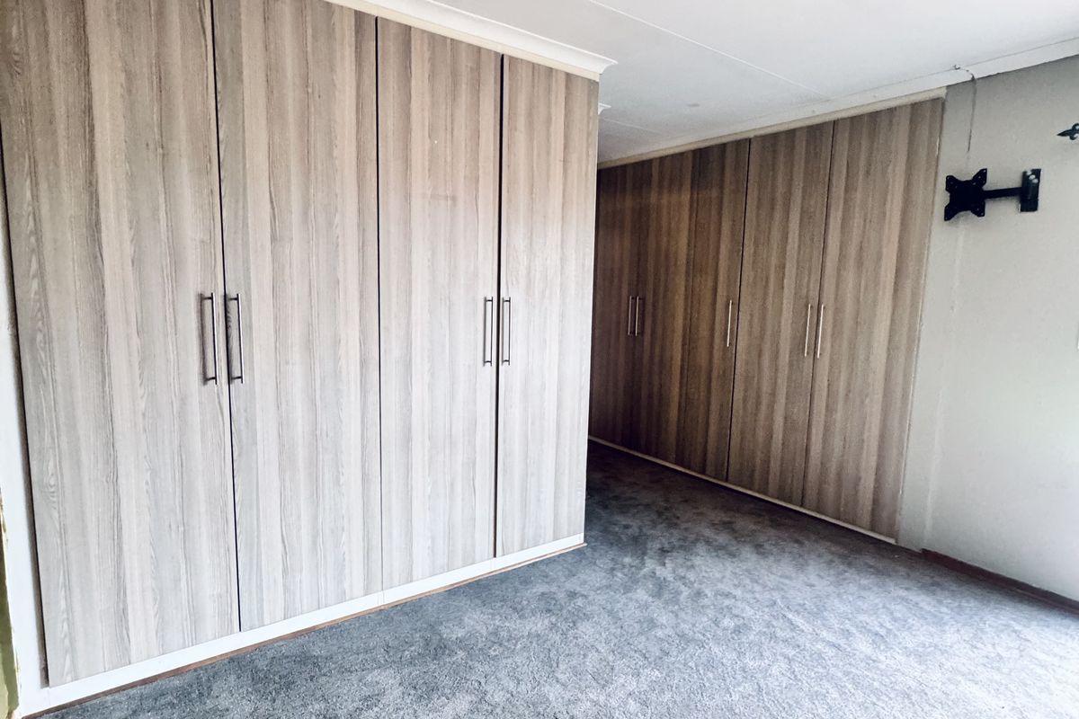 A bedroom featuring extensive built-in wooden cabinetry and grey carpeting, providing ample storage space.