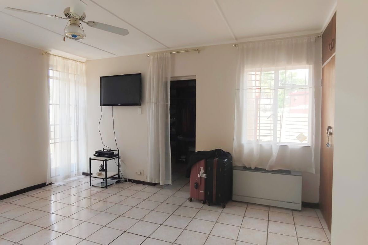 A spacious bedroom featuring tiled flooring, a ceiling fan, and built-in storage, offering a functional layout with natural light.