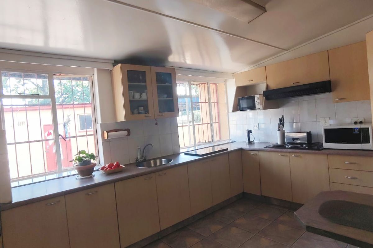 A functional kitchen featuring light wood-toned cabinetry, tiled flooring, integrated cooktop, and extractor fan, with ample natural light from large windows.