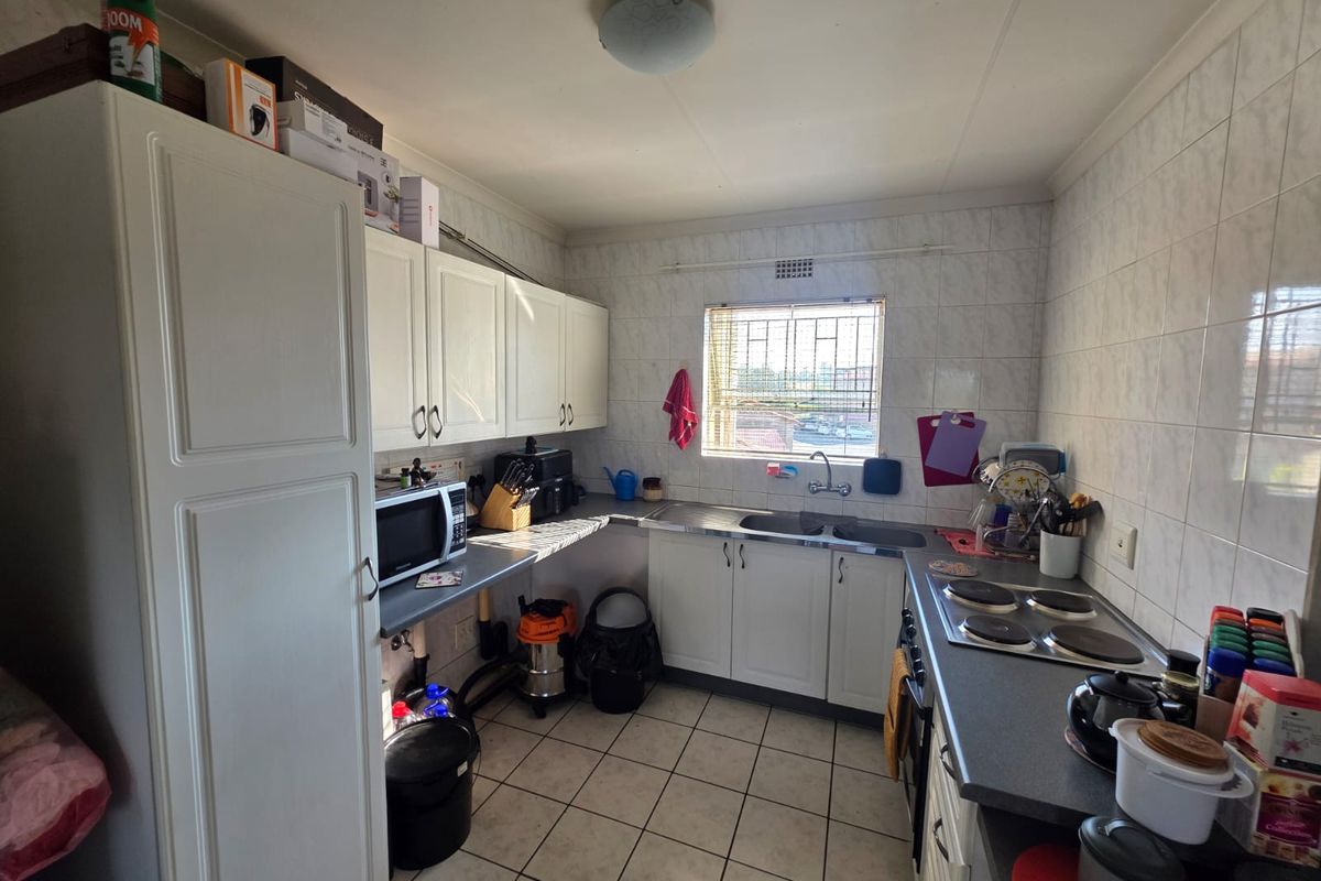 A functional kitchen featuring white cabinetry, tiled walls, a double sink, and a built-in electric hob, offering a practical layout for daily use.