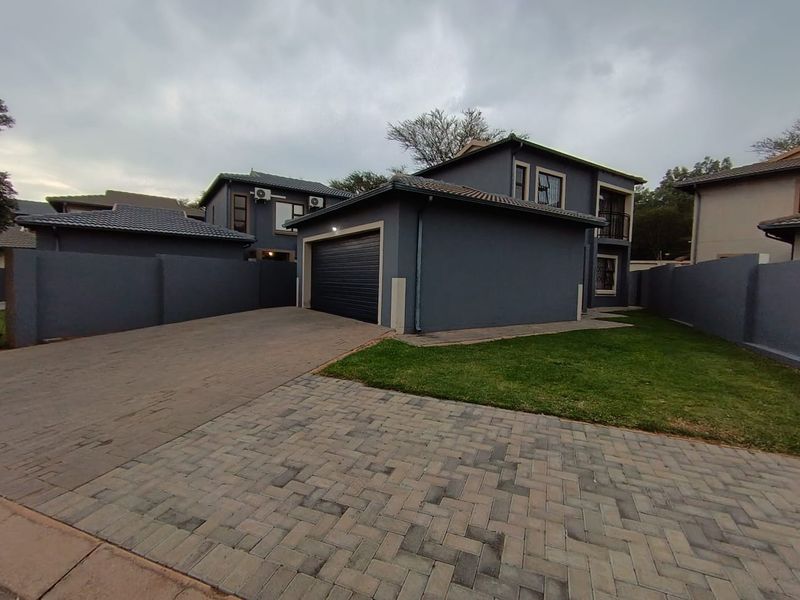 Front view of a modern double-story house featuring a paved driveway, enclosed garage, and well-maintained boundary walls.